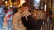 © 4kclips - A romantic couple shares a street food snack in Paris France at night The urban city background is blurred with bokeh lights creating a warm and inviting atmosphere for love and travel concepts.