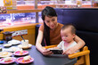© leungchopan - Mother and baby looking at phone in restaurant