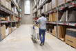 © EkaZehner - Man walking through furniture warehouse with cart and boxed furniture