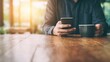 © tashechka - Person using smartphone while holding cup at wooden table in sunlight