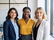 © Vasiliy - A diverse team of three professional businesswomen smiling in a modern office. Portrait of successful female colleagues representing multicultural teamwork and leadership