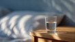 © Anastasiya Marchenko - Glass of water on wooden bedside table with soft natural light and blurred bed background in cozy bedroom setting