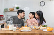 © Pormezz - happy family together. Asian parent eating breakfast with little son in the kitchen.