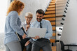 © Novak - Group of three diverse colleagues discussing a project while looking at a laptop in a modern office.