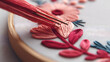 © SIMANG - Close-up of a needle with thread working on a floral embroidery pattern in an embroidery hoop, showcasing handcraft and textile artistry.