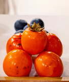 Raw Ripe Orange Persimmons on a plate over gray surface, low angle view. Copy space. Diospyros kaki, the Oriental persimmon, Chinese persimmon, Japanese persimmon or kaki persimmon, is the most widely