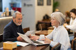 © JackF - Elderly man and woman work with documents and a laptop during a business meeting in a coffee shop.