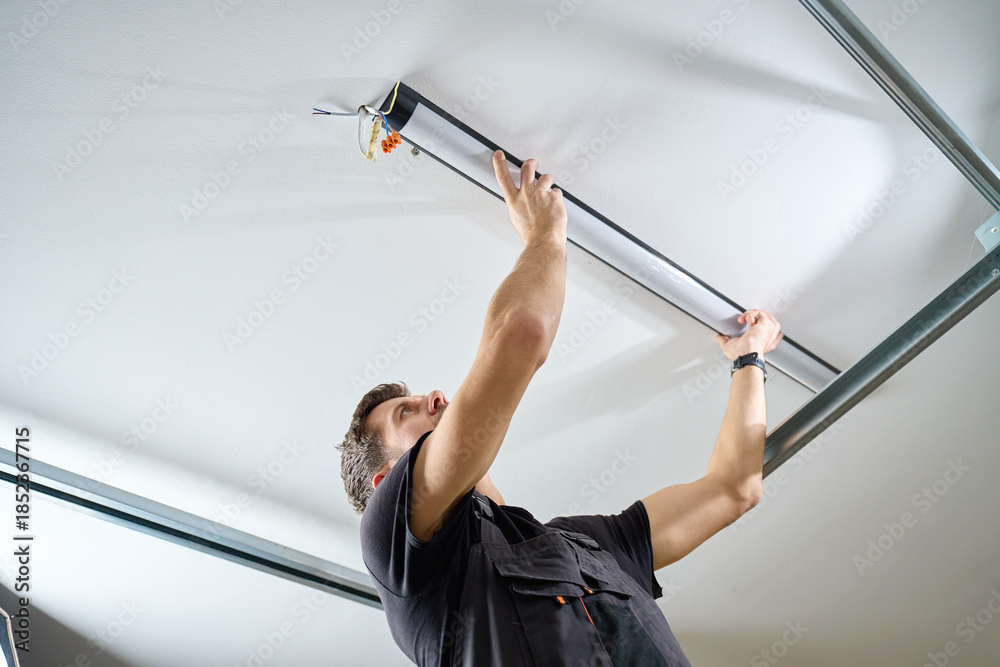 Man in workwear installing a linear LED light fixture on the ceiling ...