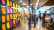 © florynstudio3 - A wall of colorful sticky notes on a glass partition in a modern office, blurred figures of people are visible