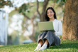 © Phimwilai - Young woman remotely working on laptop in park