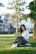 © Phimwilai - Young woman working remotely using laptop in green park