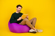 © deagreez - Young man reads a yellow book while lounging on a purple bean bag in a bright studio for a casual lifestyle image