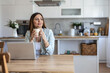 © Jelena Stanojkovic - Dreamy young businesswoman using laptop and holding coffee cup enjoying freelance work sitting at desk indoors. Female entrepreneur having hot drink thinking looking aside at workplace.
