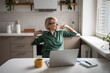 © DimaBerlin - Smiling middle aged businesswoman stretching in chair during work on laptop, taking break to warm up, looks at window while working on remote from home in kitchen Female enjoys small break at work.
