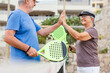 © Daniel - Senior couple playing paddle tennis or padel, outdoors in padel court enjoying and having fun together. Mature woman and old man high five after finish game