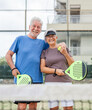 © Daniel - Portrait of couple of mature people playing padel game outdoors in a paddle tennis court together. Old man embracing mature woman teammate looking camera