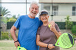 © Daniel - Portrait of couple of mature people playing padel game outdoors in a paddle tennis court together. Old man embracing mature woman teammate looking camera