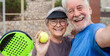 © Daniel - Old senior couple outdoors in paddle tennis court smiling and looking at the camera taking a selfie picture together playing padel. Active mature people concept