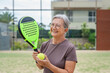 © Daniel - One old mature senior woman in padel court outdoors looking at the camera having fun holding paddle tennis racquet smiling and enjoying after game