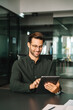 © Stock 4 You - Smiling European 30s trade manager looking at digital tablet screen sitting at desk in office. Executive professional man working online using computer for financial business banking work. Vertical