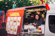 © Maskot - Smiling young female owner looking away while leaning on food truck window