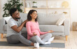 © Prostock-studio - Loving African American husband massaging his meditating pregnant wife, sitting on floor at living room, exercising together, copy space