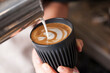 © n3moh3ro - Barista pouring milk to create latte art in a black reusable coffee cup