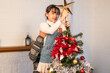 © Kawee - Asian father holding young daughter place star on top of Christmas tree.