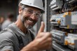 © Zabi - Smiling male electrician wearing safety helmet and goggles gives a thumbs up while inspecting electrical panel with wires and circuits, representing a job well done in a modern industrial setting.