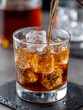 © SashaMagic - Close-up of whiskey being poured into a glass with ice cubes.