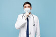 © ViDi Studio - Young male doctor man wears white medical gown suit sterile mask work in hospital clinic say hush be quiet finger on lips shhh gesture isolated on plain blue background. Healthcare medicine concept.