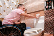 © Alex - A man in a wheelchair leans on a toilet cistern.