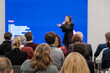 © Anton Gvozdikov - Audience listening to a speaker in a conference setting with a bright blue screen. Attentive crowd in rows creating a professional event mood.