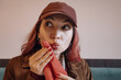 © EdNurg - Young woman with red hair and a cap, cleaning her mouth with a napkin and looking sideways with a playful expression