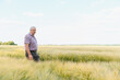 © Serhii - Senior agronomist walking and inspecting wheat field in summer day