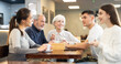 © JackF - Young man and women sit at a table in a coffee shop and actively communicate with the older generation, they discuss family plans. Elderly people met with grandchildren