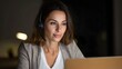 © Thares2020 - A professional woman wearing a headset concentrates while working on a laptop in a dimly lit environment late at night