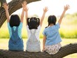 © AdityaGM - Three Little Girls Sitting on Tree Branch with Hands Up. Generative Ai
