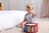 Cute little boy playing with toy drum on floor at home