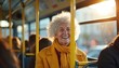 © Maryna - Smiling senior woman with curly hair rides on bus. Elderly lady wears yellow coat and scarf, enjoys daytime journey. Passenger looks out window at city lights.