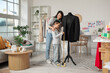 © Pixel-Shot - Happy Asian mother and her daughter taking measurements of black jacket on mannequin in sewing studio