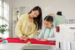 © Pixel-Shot - Happy Asian mother and her daughter drawing sewing pattern with chalks in workshop