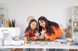 © Pixel-Shot - Happy Asian mother and her daughter with handmade toys in sewing studio