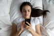 © fizkes - Lonely night texting. View from above upset depressed young woman lying in bed frown read smartphone message feel sadness anxiety solitude jealous struggle with relationship problems in online chat