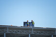 © Nattawit - Two worker who wearing full safety PPE are installing solar cell panel on the factory rooftop with blue sky background. Industrial working scene.