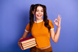 © deagreez - Young female student with book smiles and shows ok gesture against violet background