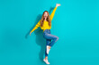 © deagreez - Young woman jumping with joy wearing a yellow sweater jeans and white sneakers against a bright blue background