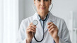 © RATUL HASAN - Professional smiling female doctor in white coat holding medical stethoscope in hands, ready for check up, standing in bright hospital or clinic room