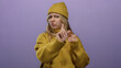 © Krakenimages.com - Woman blonde wearing yellow sweater and hat holding cookie against isolated purple background showing disapproval with finger gesture suggesting disagreement or denial