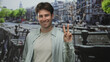 © Krakenimages.com - Man showing peace sign with hand on street by amsterdam canal, smiling and relaxed; cheerful travel.